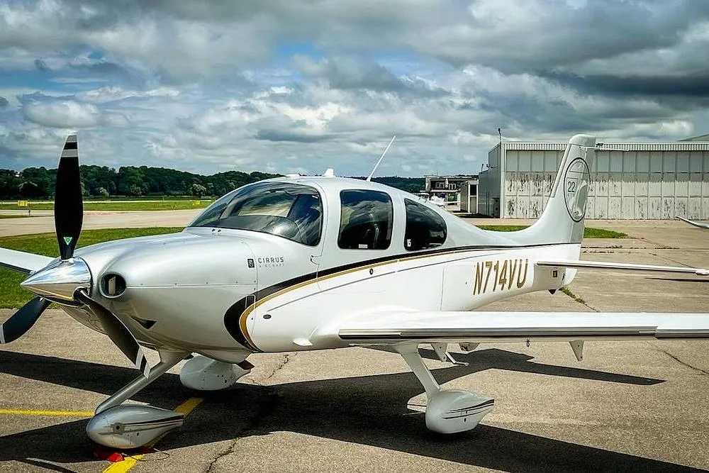 A white and silver Cirrus SR22 aircraft with gold and black accents, registration N714VU, parked on an airfield under a cloudy sky.