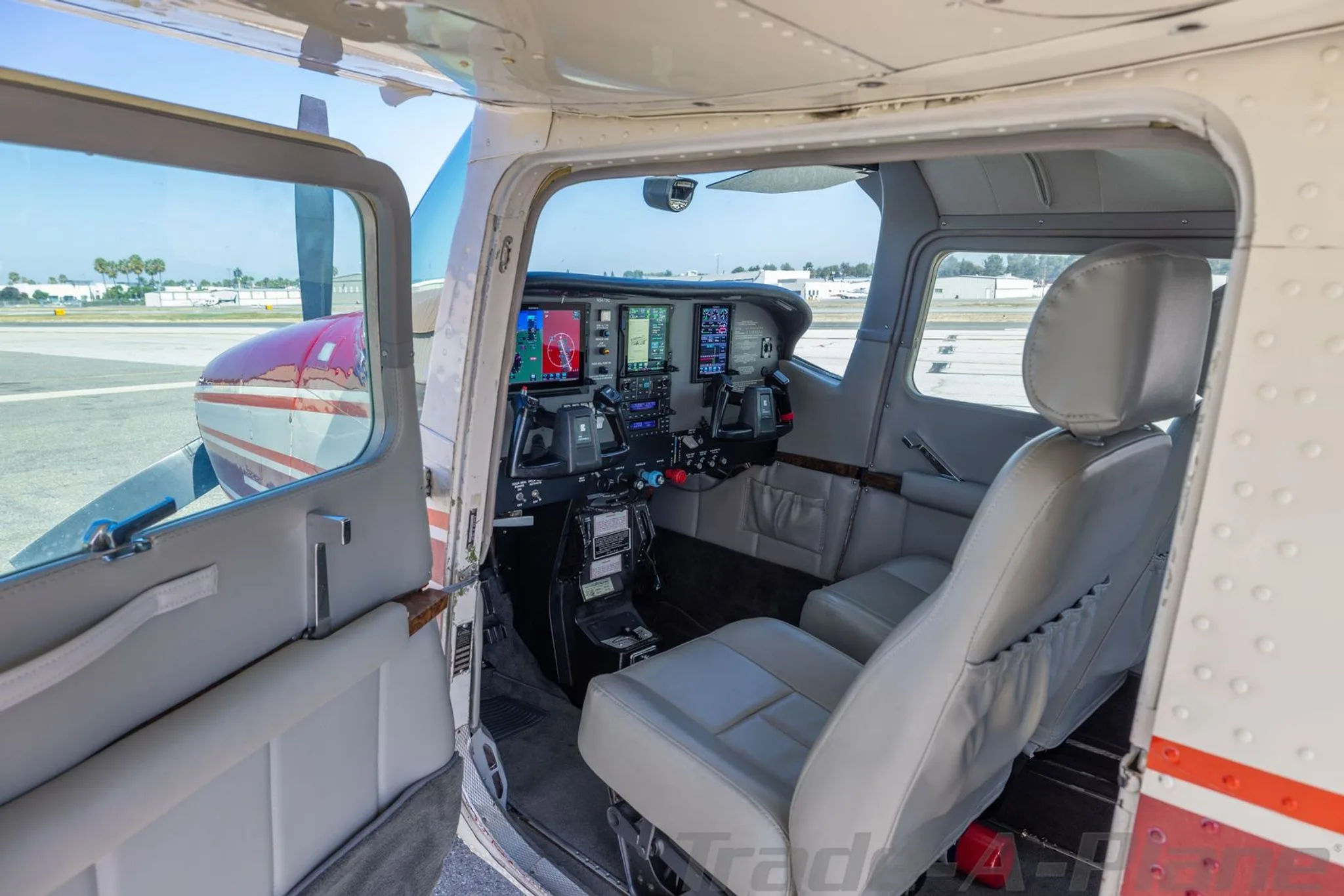 The cockpit of a Cessna 210 Centurion aircraft with modern glass panel displays, viewed through an open door.