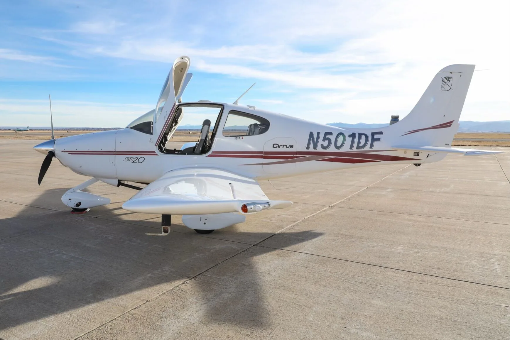 A white Cirrus SR20 aircraft with red stripes, tail number N501DF, parked on an airfield with its gull-wing doors open.