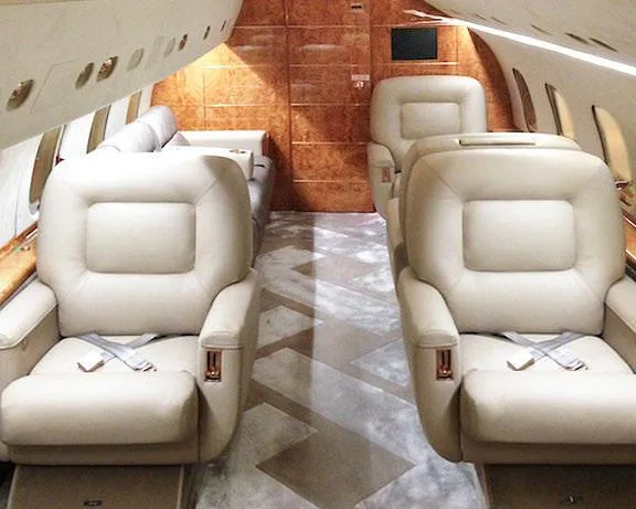 The luxurious cabin interior of a private jet with two rows of beige leather seats and wood paneling.