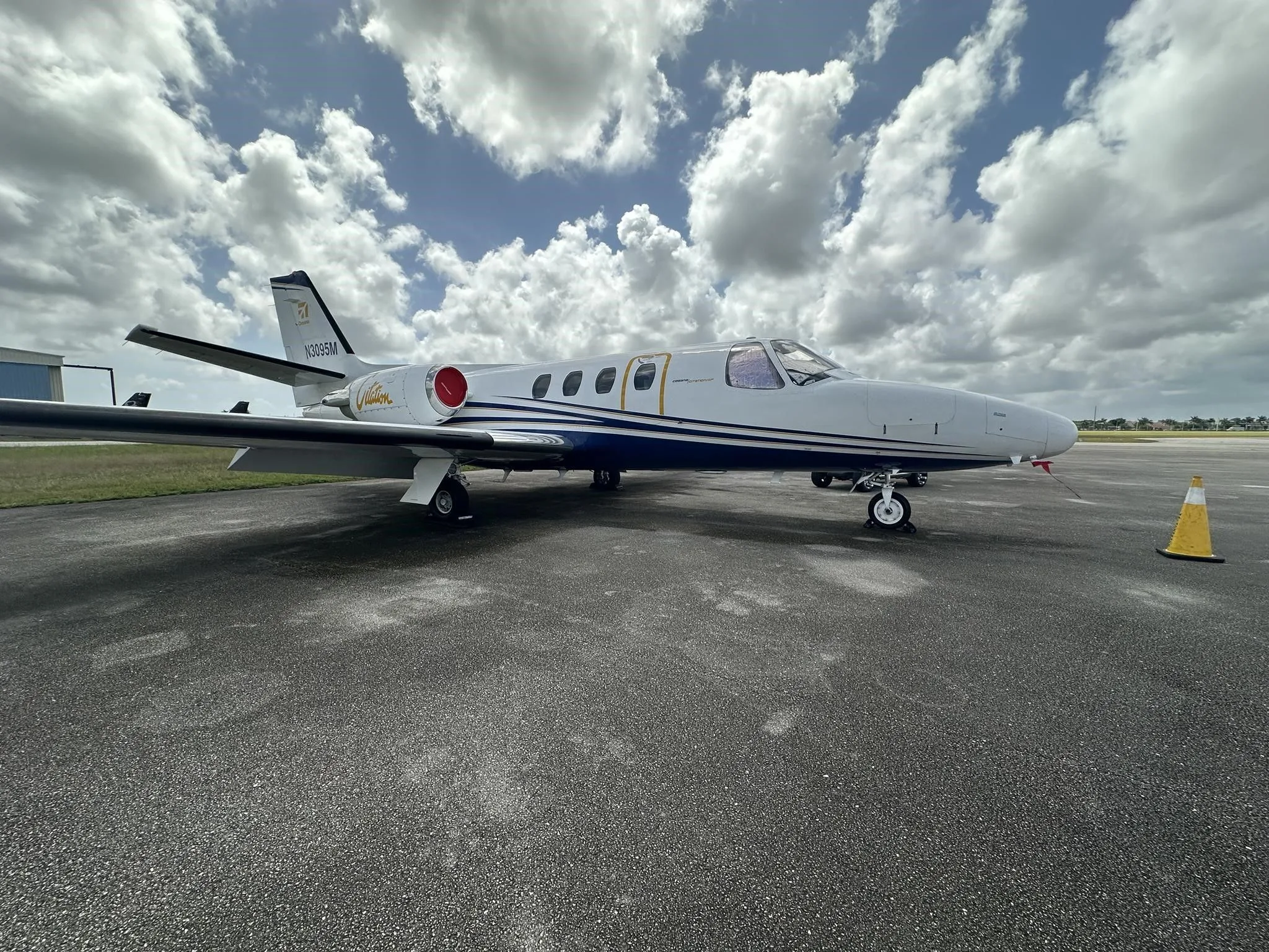 A white and blue Cessna Citation jet (N3095M) parked on an asphalt ramp under a cloudy sky.