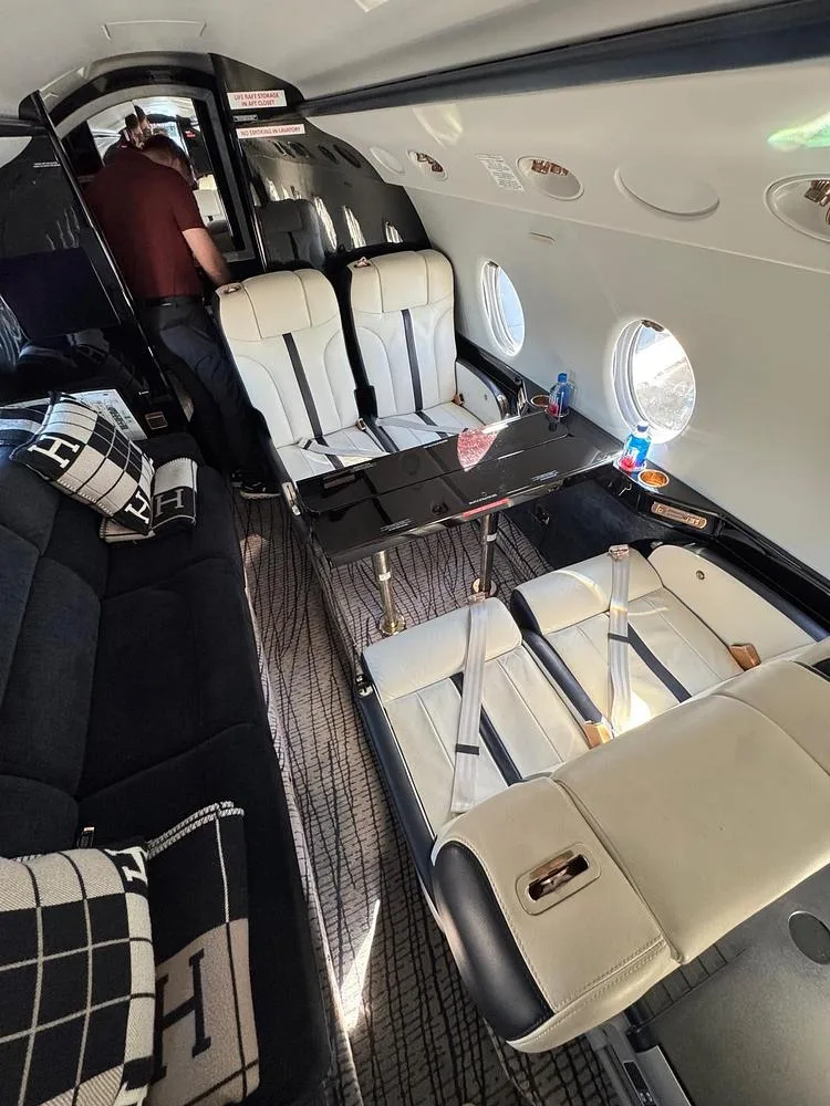 An overhead view of the private jet's cabin, showing cream and black seats, a black couch, and a table with drinks.