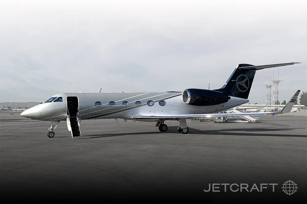 A silver and dark blue Gulfstream G450 business jet with its main door open and stairs deployed, parked on a tarmac.