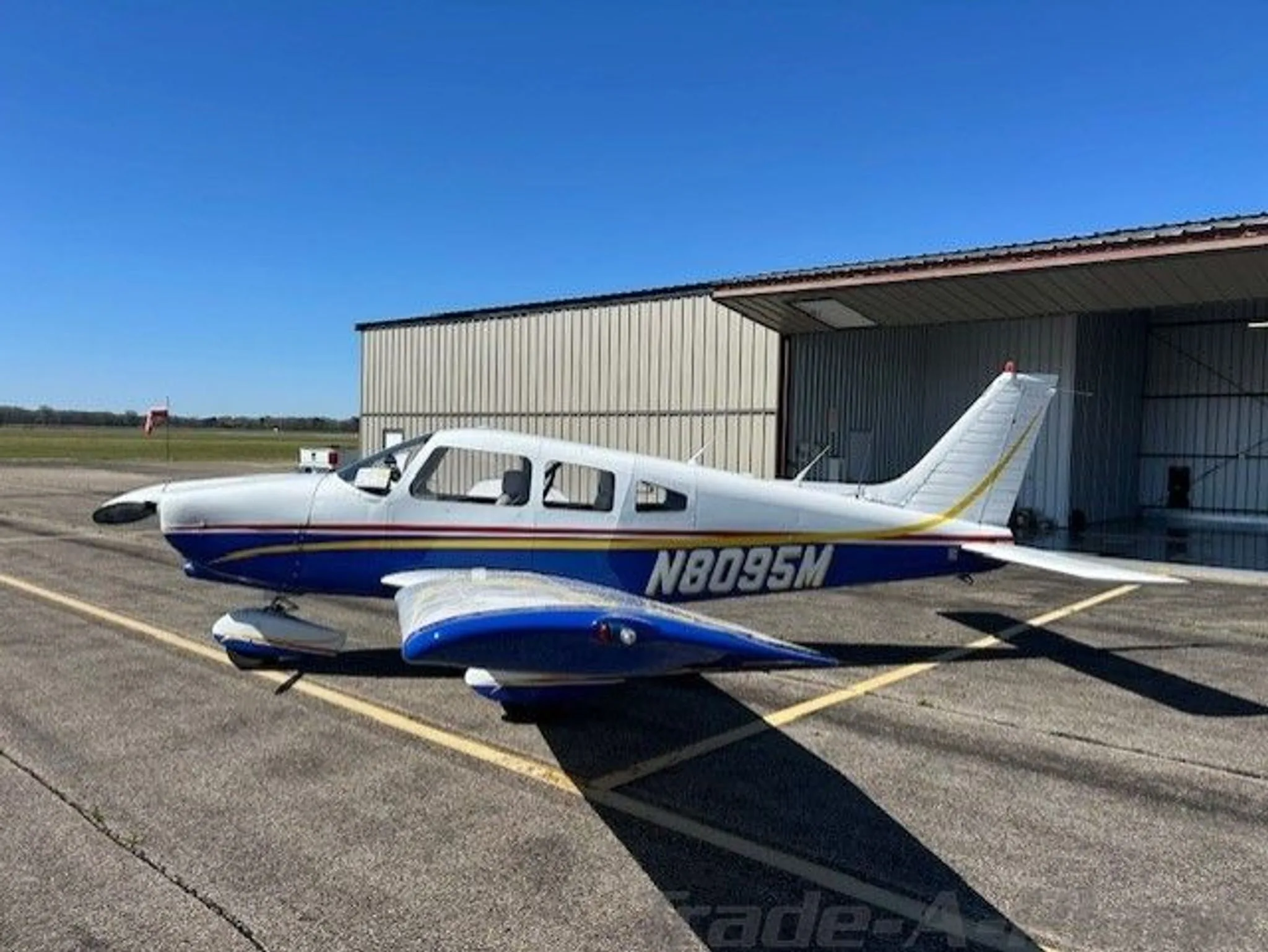 A three-quarter front view of a white and blue Piper Cherokee aircraft with N8095M registration on an airfield.