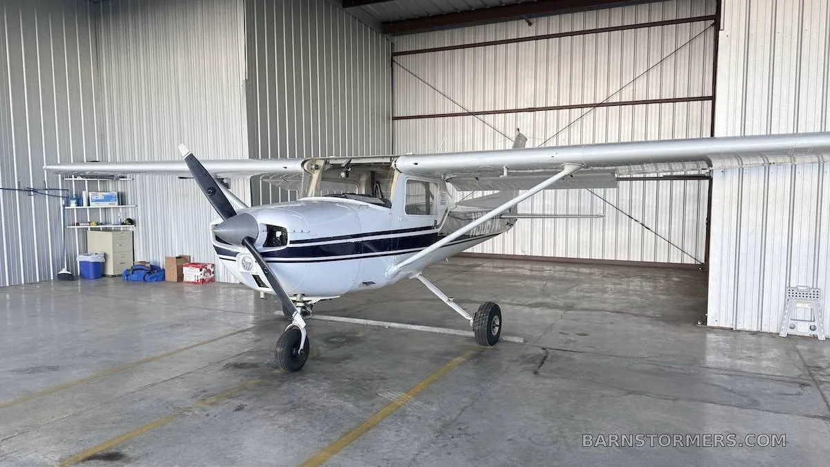 A white single-engine propeller aircraft with blue stripes parked inside a hangar.
