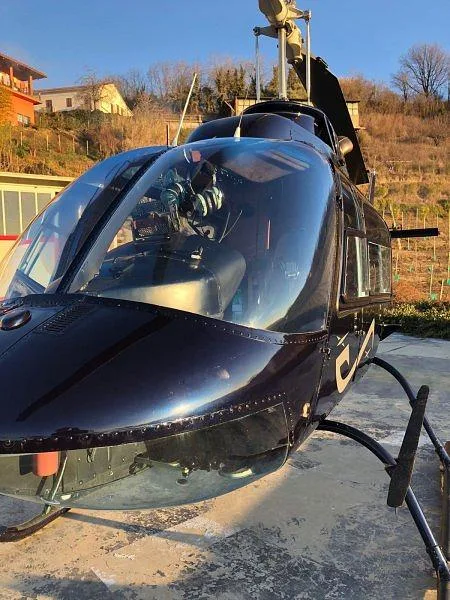 A close-up view of the front cockpit and nose of a dark blue Bell 206 helicopter parked on a concrete pad.