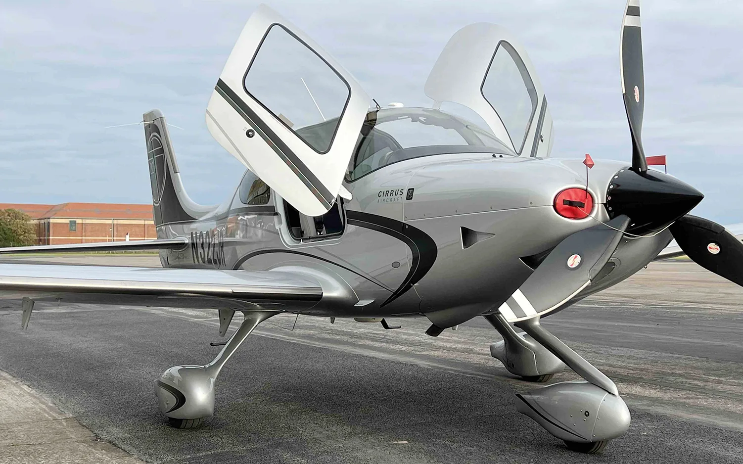 A silver Cirrus SR22 aircraft with registration N322JR and open doors is shown from a low angle on an airfield.