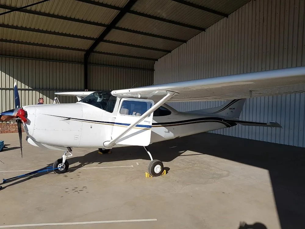 A white Cessna Skylane aircraft with blue and gold stripes parked inside a hangar.