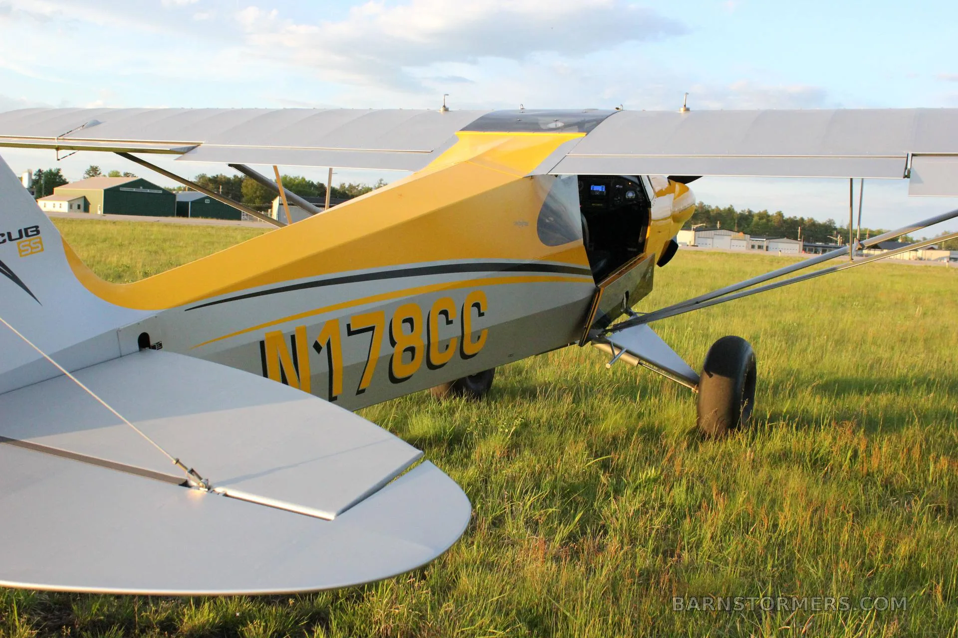 A close-up view of the tail and fuselage of a yellow and grey Carbon Cub aircraft (N178CC) on a grassy field.