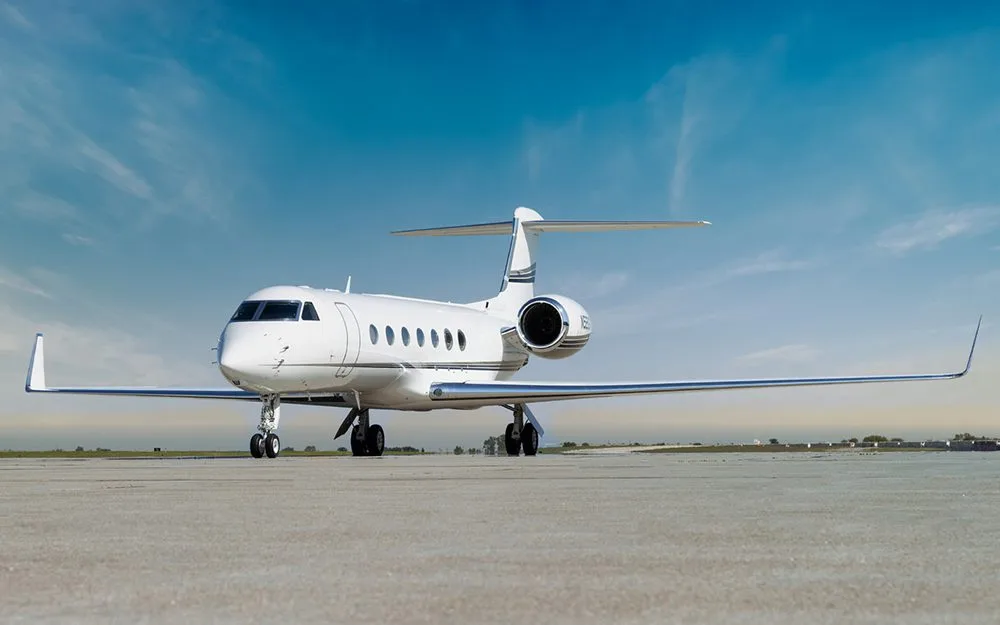 A white Gulfstream G550 business jet with a black stripe on the tail, viewed from the front on a tarmac.
