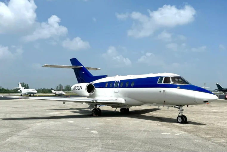 A white and blue business jet, N750FA, parked on an airport tarmac under a partly cloudy sky.
