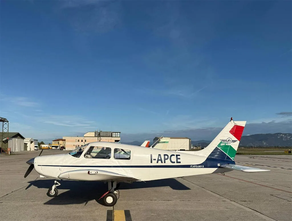 A white single-engine propeller aircraft with "I-APCE" registration and "Aero Club Brescia" logo on the tail, parked on an airfield under a blue sky.