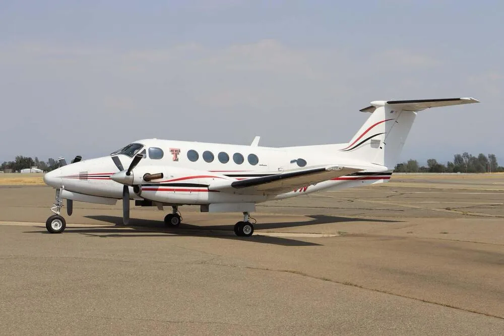 A white Beechcraft King Air with red and black stripes parked on an airport tarmac.