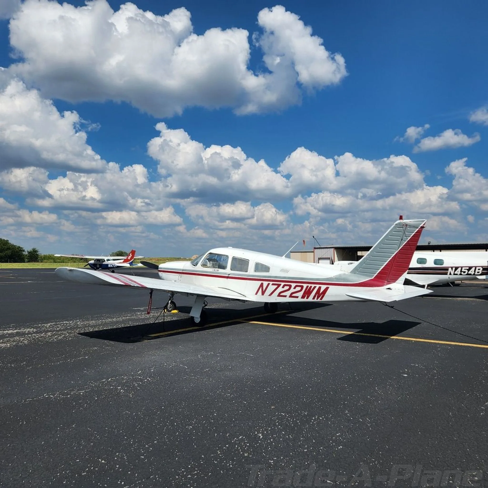 A white Piper Cherokee with red and grey stripes, registration N722WM, parked on an asphalt ramp.