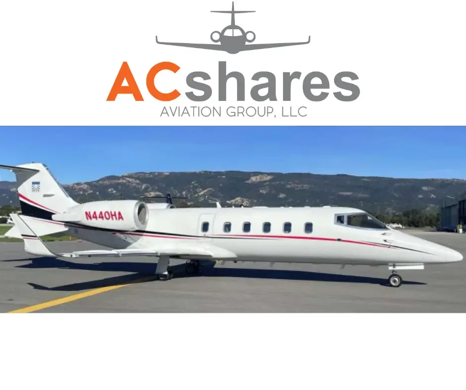 A white private jet with red and black stripes is parked on an airport tarmac with mountains in the background.