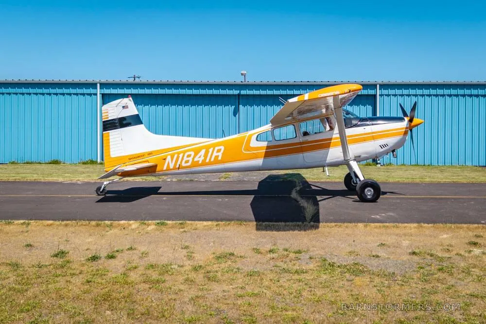 A side view of a white and orange single-engine propeller aircraft with tail number N1841R parked on an asphalt ramp.