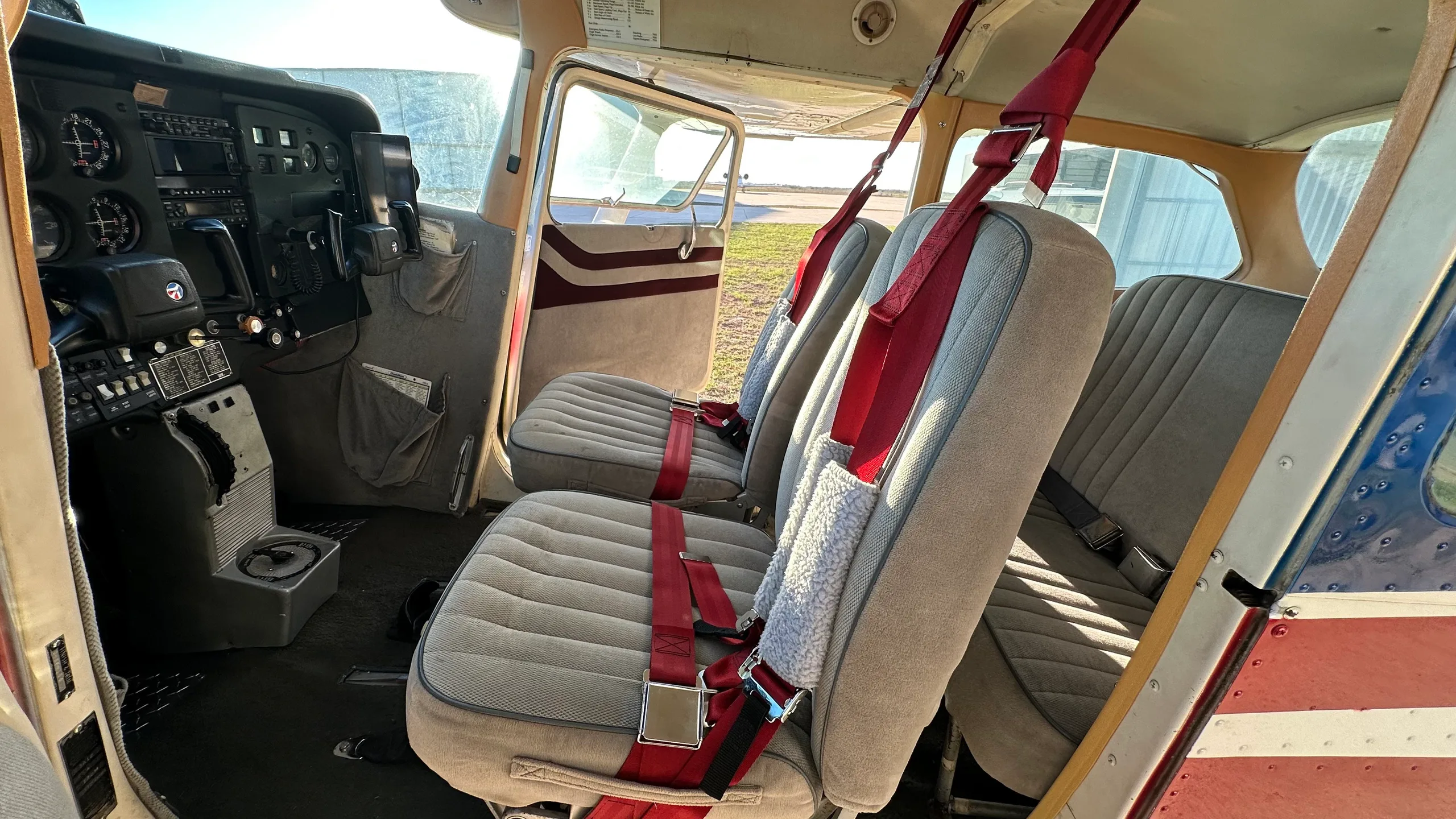 The interior of a small aircraft cabin showing the front and rear seats with red seatbelts and a view towards the cockpit.