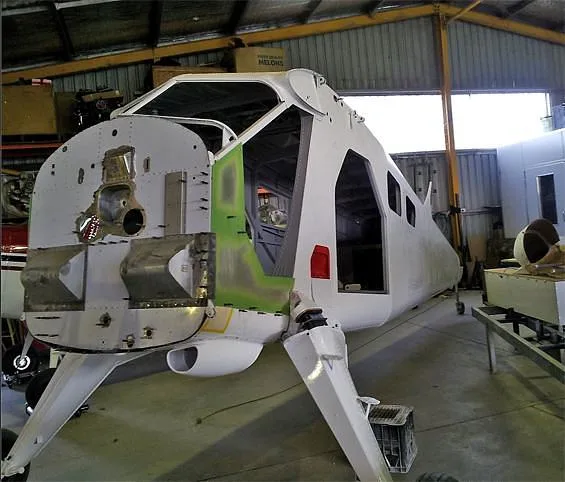 A white aircraft fuselage with its nose section open, showing internal structure, in a hangar.