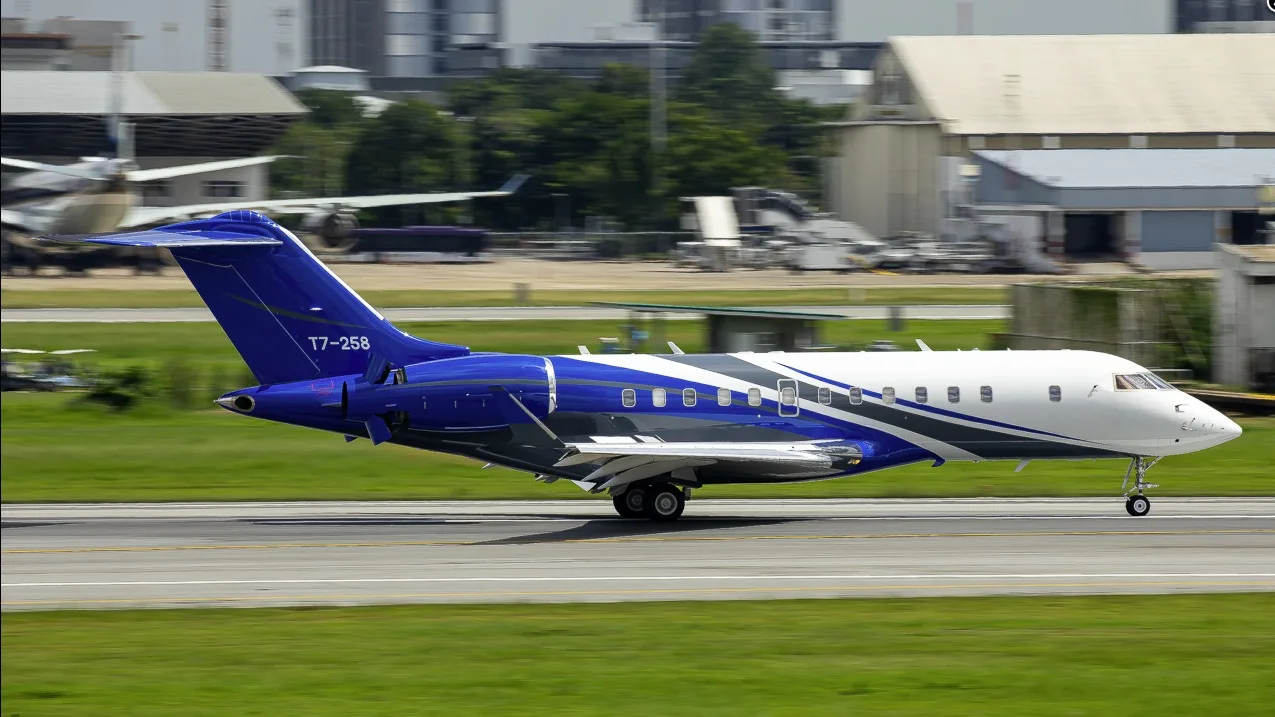 A blue, white, and grey business jet, registration T7-258, is seen taxiing on an airport runway with blurred background buildings.