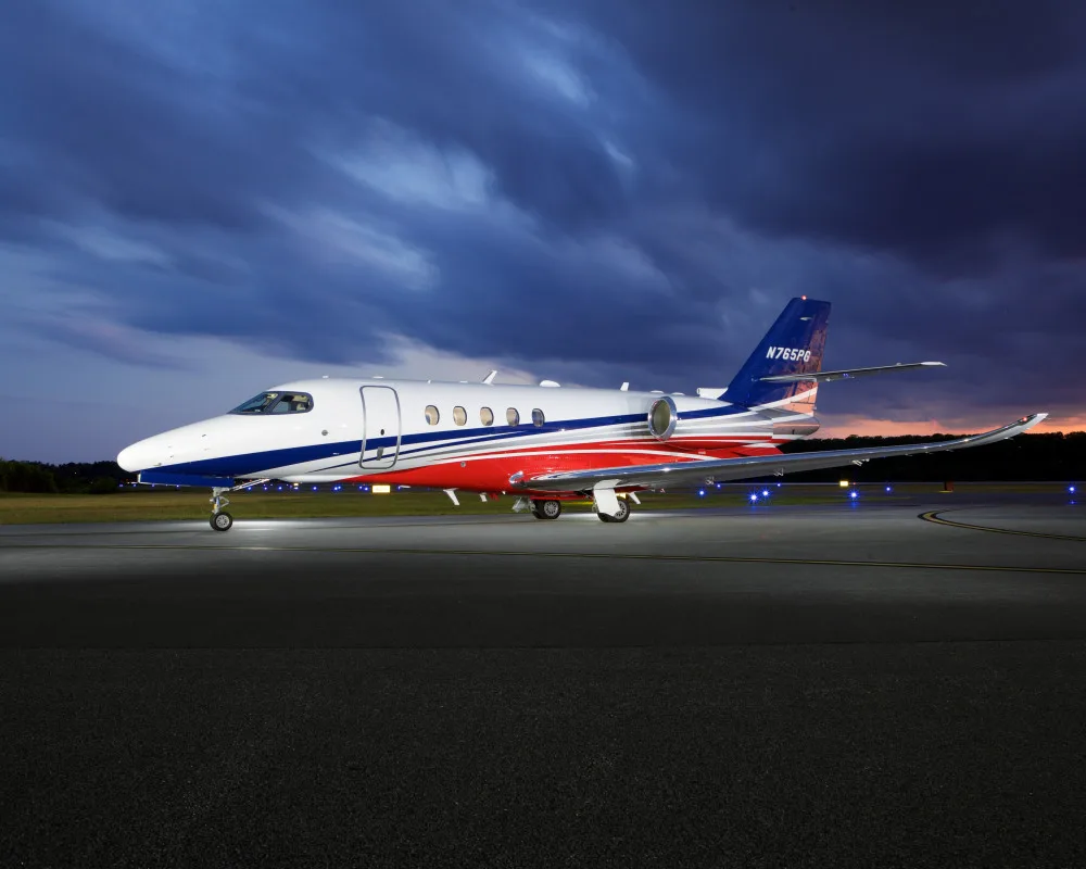 A white, red, and blue private jet (N765PG) is parked on an airport tarmac at dusk.