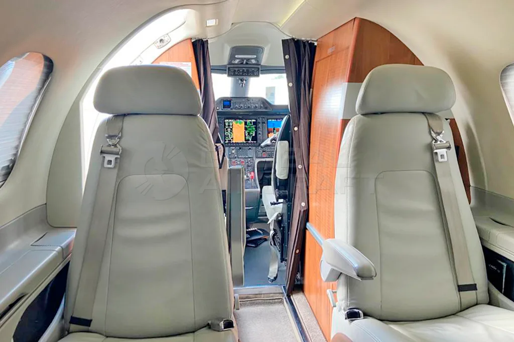 The interior cabin of an Embraer Phenom 100, showing two light grey seats facing the cockpit.