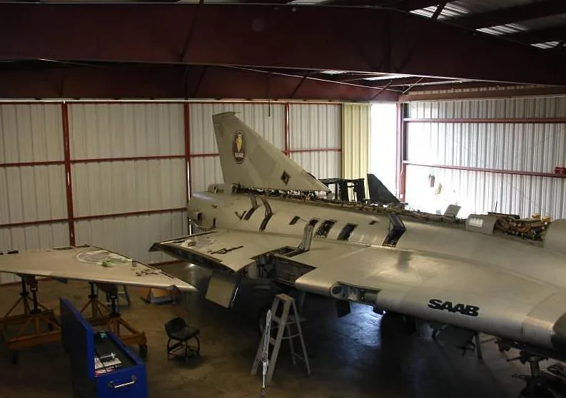 A rear view of a disassembled Saab Draken aircraft with its tail section and fuselage exposed in a hangar.