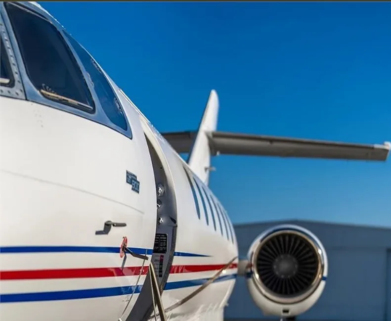 A close-up view of the front fuselage and engine of a white business jet with an open passenger door.