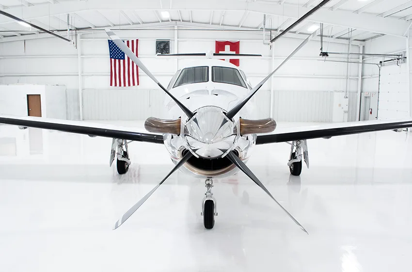 A side view of the fuselage of a white Pilatus PC-12NG aircraft, showing its gray and red stripe livery and cabin windows.