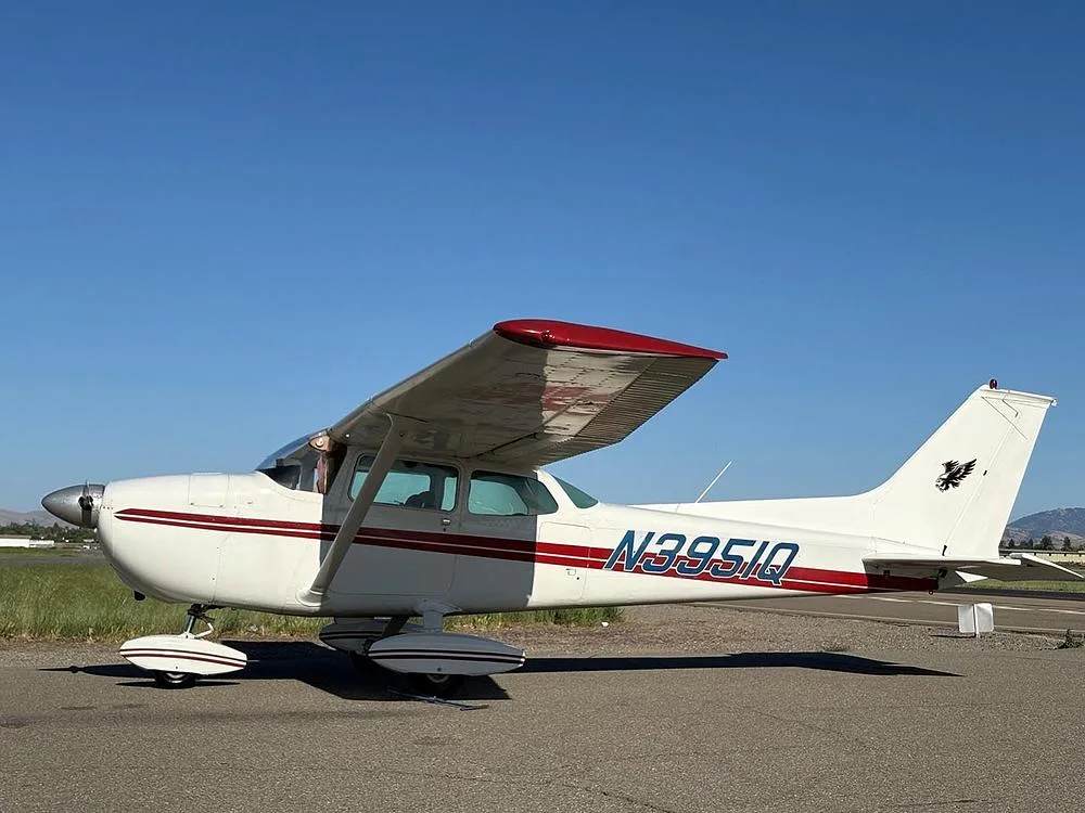 A white Cessna aircraft with red stripes and N3951Q registration parked on an airfield under a clear blue sky.