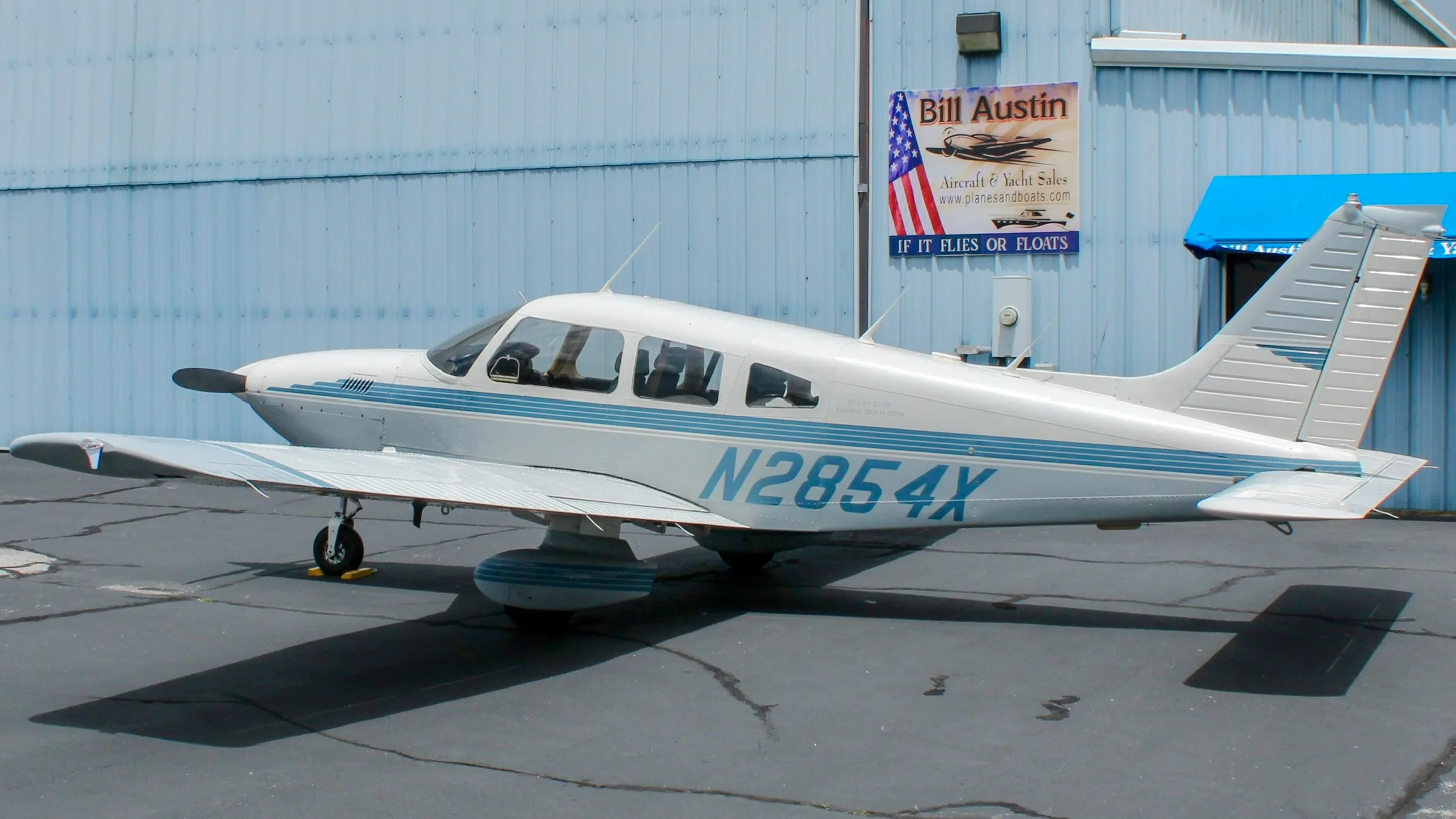 A side view of a white and blue Piper Cherokee aircraft, registration N2854X, parked on an asphalt ramp.