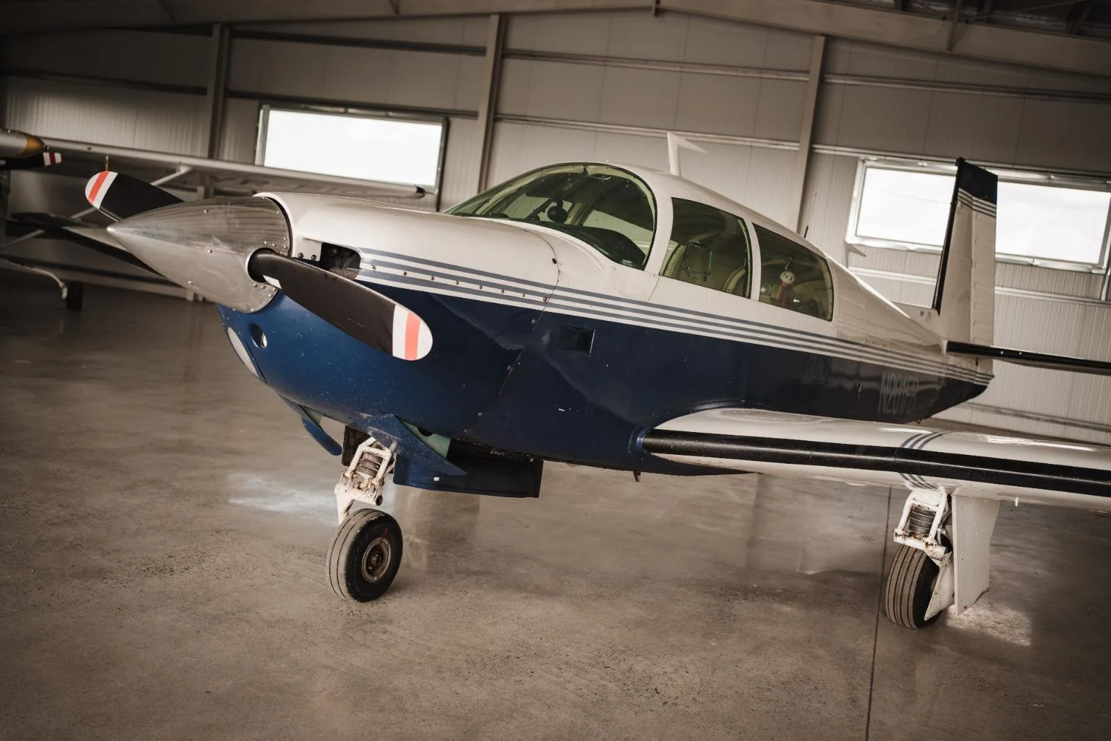 A close-up view of the front-right side of a blue and white single-engine aircraft inside a hangar.
