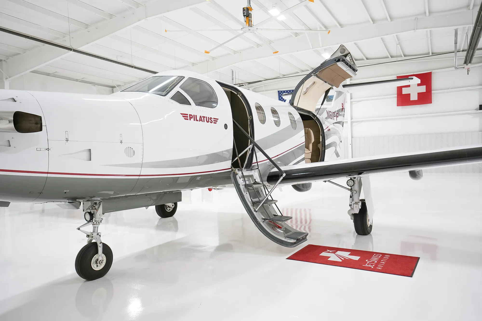 The front-right side of a Pilatus PC-12 aircraft, N61FP, with its main cabin door open and stairs extended, inside a white hangar.