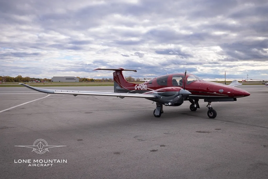 A red and grey Diamond DA62 aircraft with registration C-FCRQ parked on an airfield, viewed from the front-side.