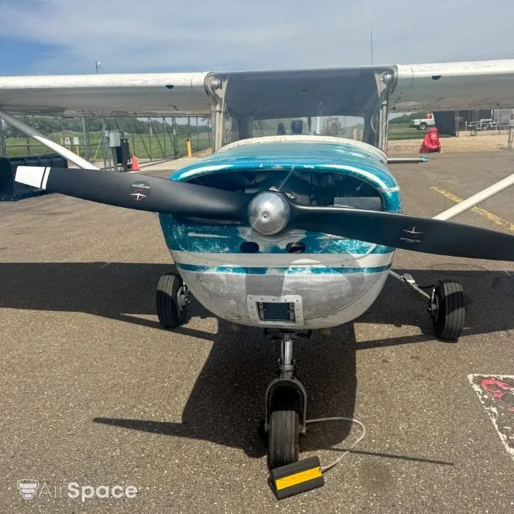 Front view of a Cessna 150 with a weathered blue and white paint scheme, parked on an asphalt ramp.