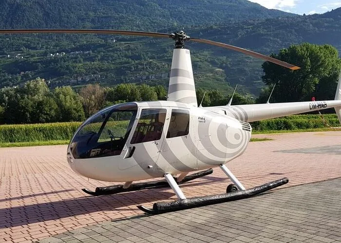 Robinson R44 helicopter with a gray and white swirl paint scheme parked on a brick surface.