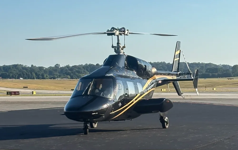 A black Bell 430 helicopter with gold stripes on an airfield under a clear sky.