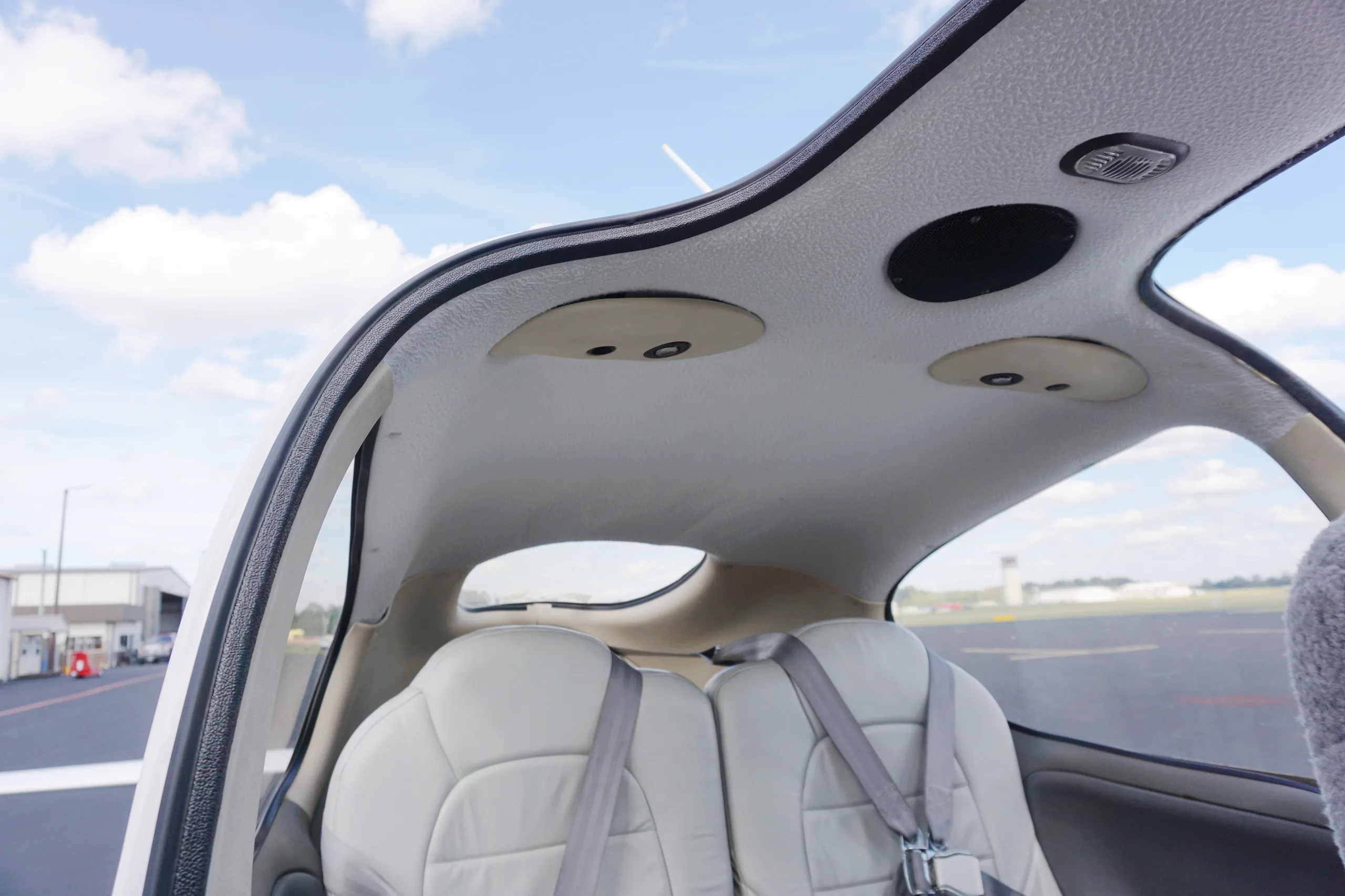 View of the light gray rear cabin seats and ceiling of a Cirrus SR22, looking out to an airport tarmac.