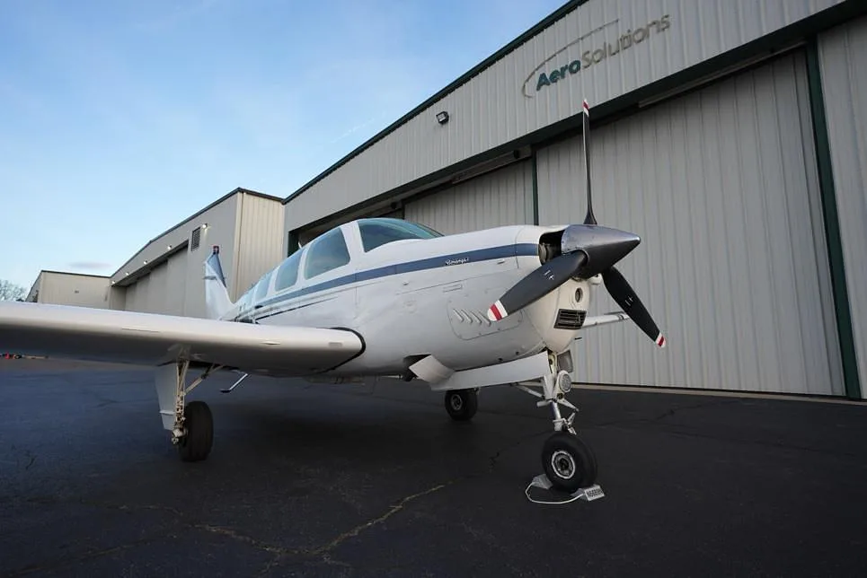 A front view of the white Beechcraft Bonanza with blue and gray stripes, registration N6689N, parked on an asphalt ramp.