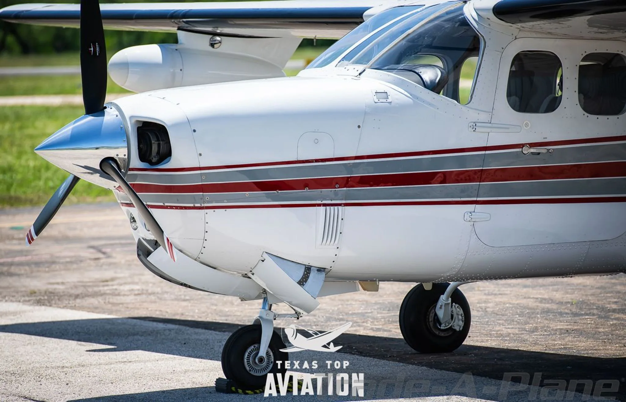 A close-up of the front section of a white Cessna 210 Centurion (N210LA), showing the propeller and nose gear.