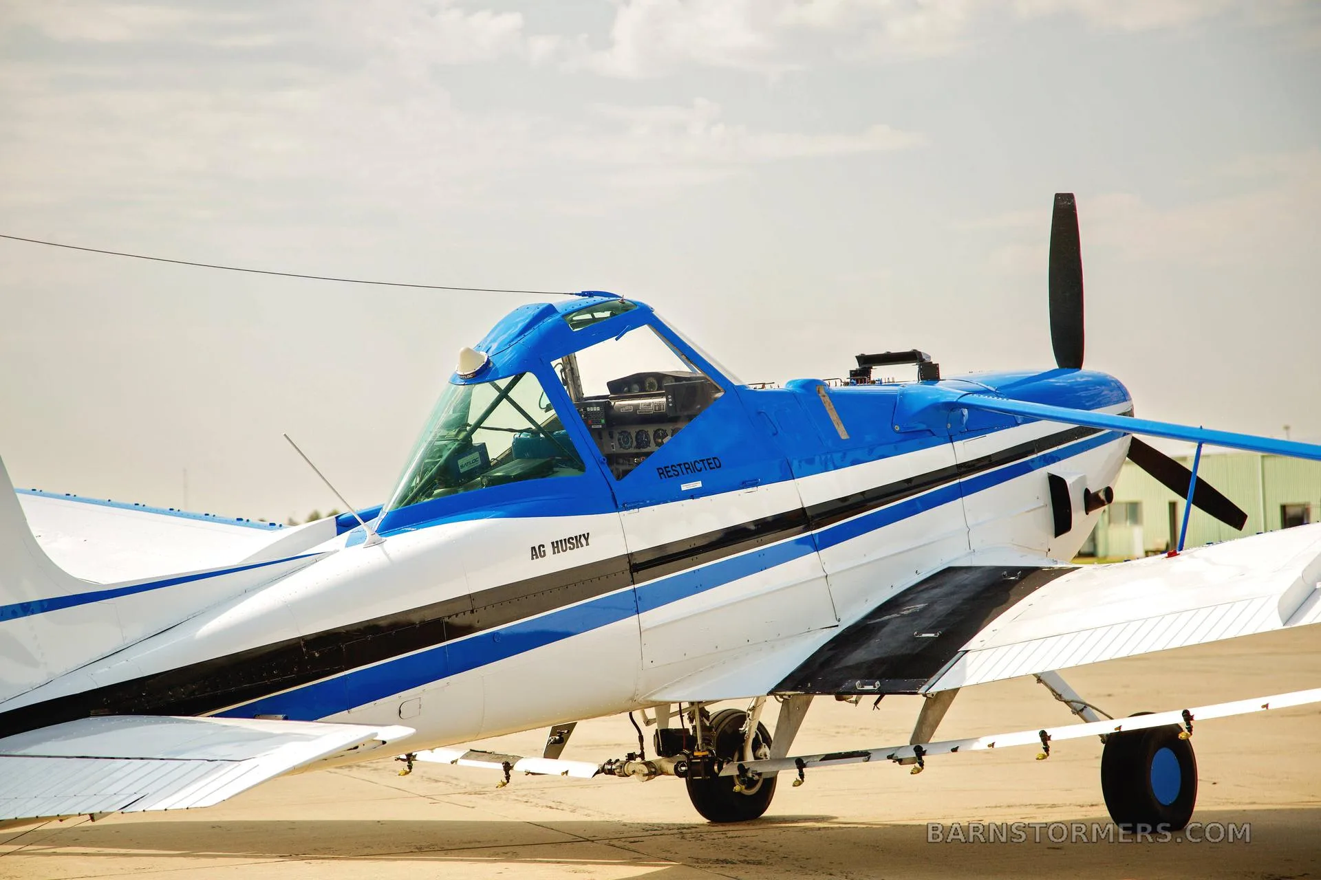 A close-up view of the front-left side of a white and blue Cessna Ag Husky agricultural aircraft, showing the cockpit and propeller.