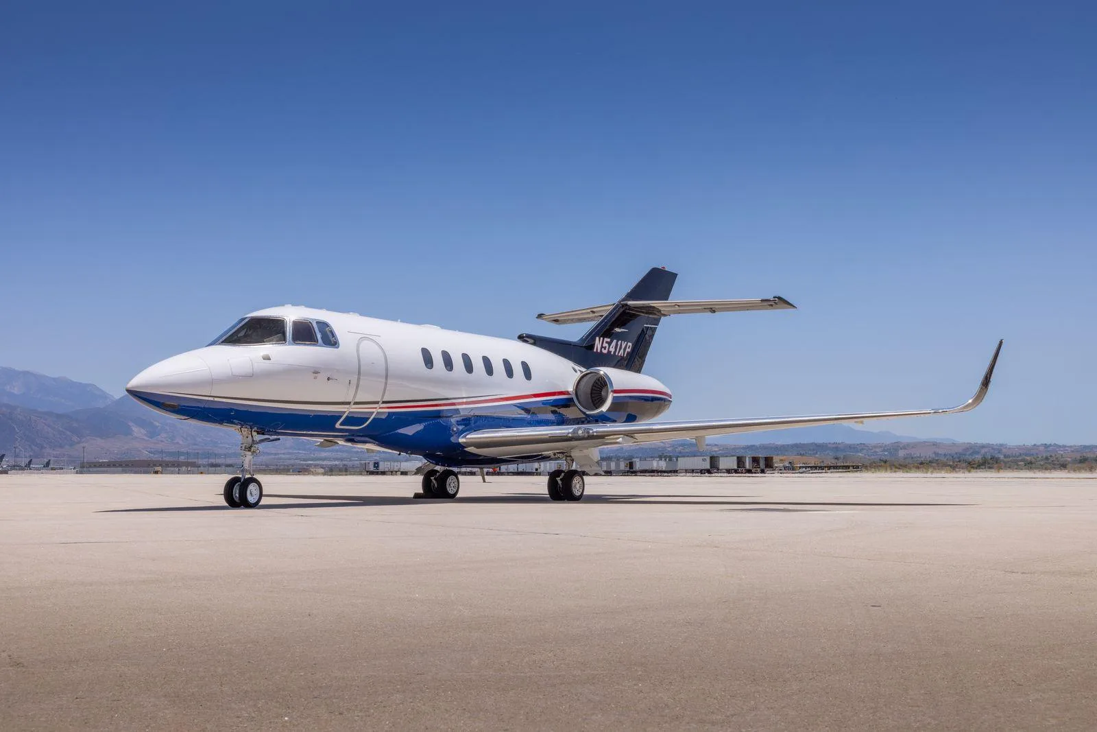A Hawker 800XP business jet (N541XP) with blue and red stripes on an airfield under a clear sky.
