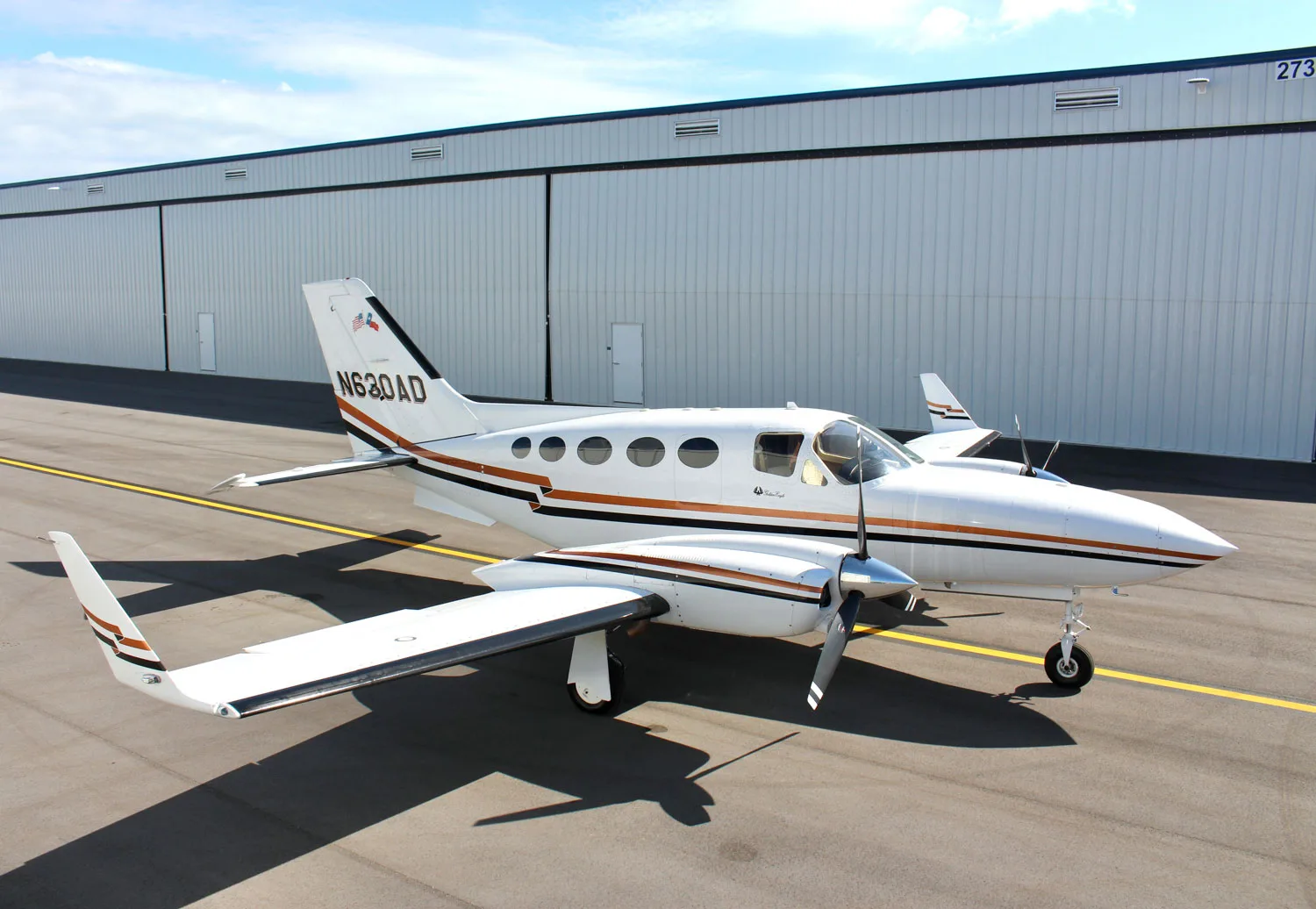 A white and brown twin-engine aircraft, N630AD, parked on the tarmac in front of a hangar.