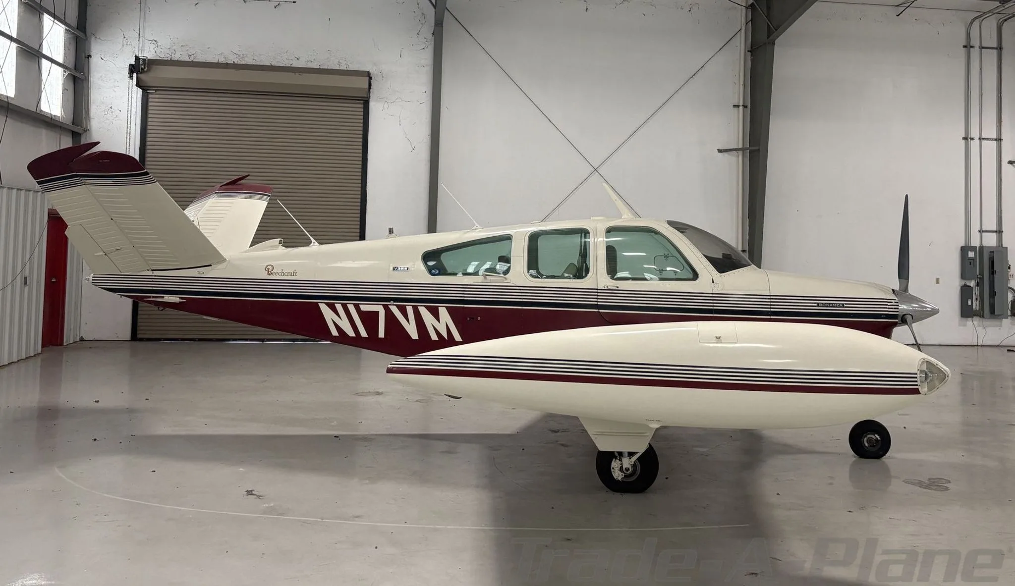 A white and maroon Beechcraft Bonanza N17VM parked inside a hangar, viewed from the left side.