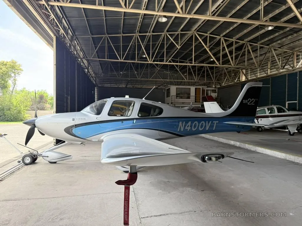 A three-quarter front view of a white and blue Cirrus SR22 aircraft, registration N400VT, parked in a hangar.