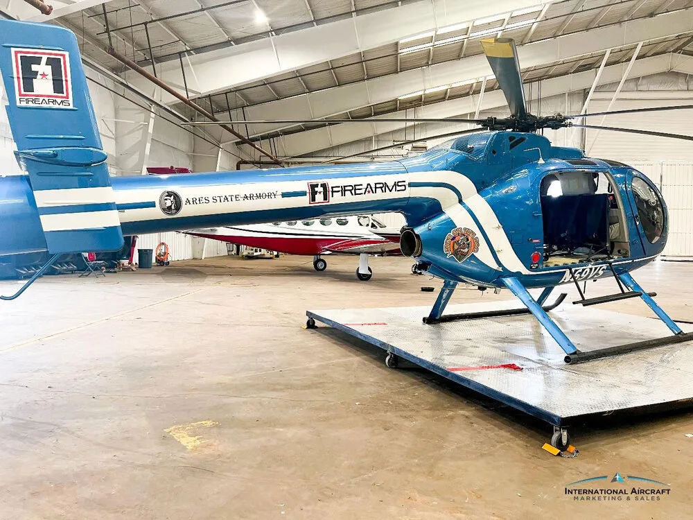 A blue N69VS helicopter with white stripes and F1 FIREARMS branding, parked on a platform in a hangar.