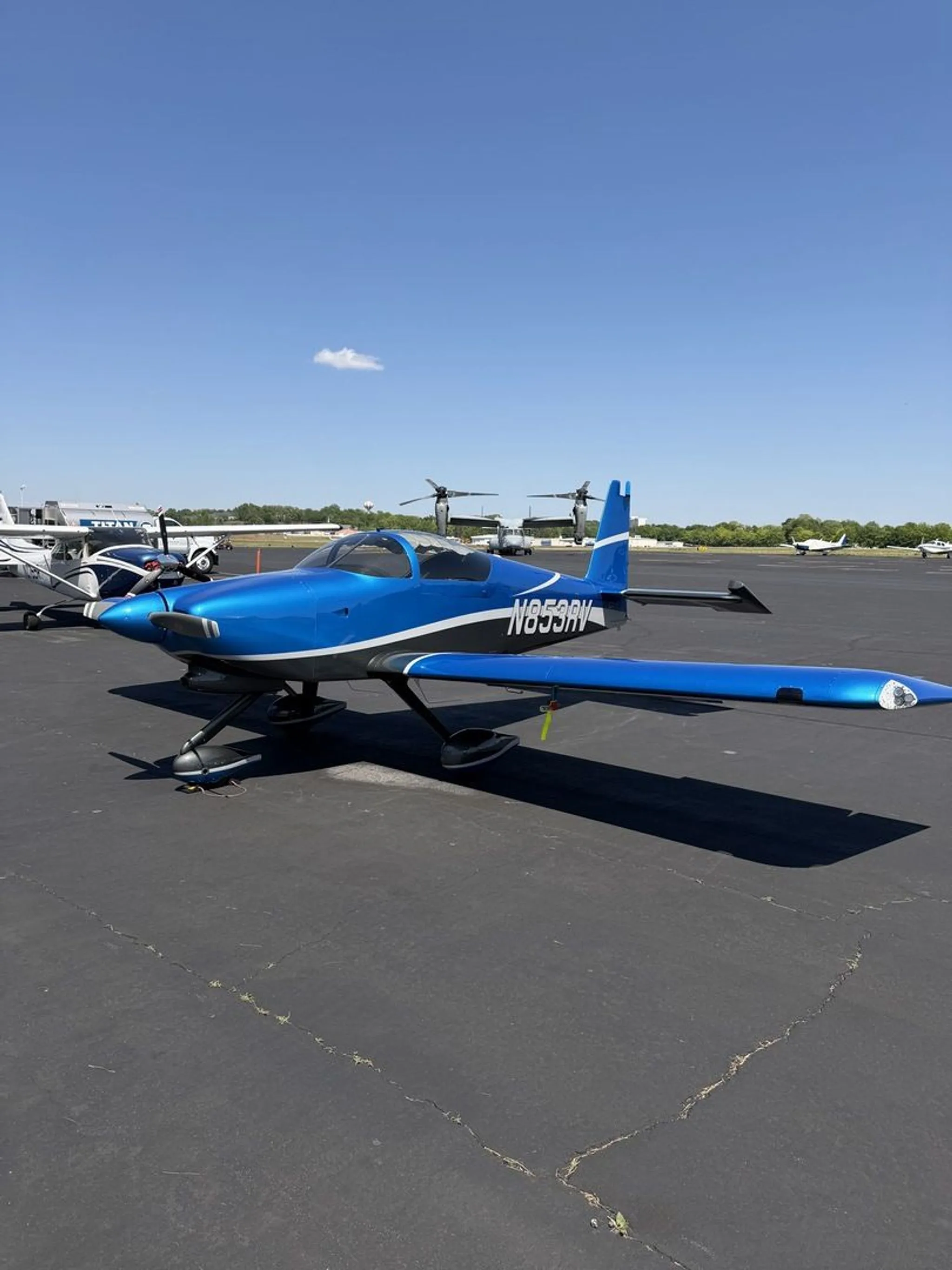 A blue and grey N853RV aircraft parked on an airfield under a clear blue sky.