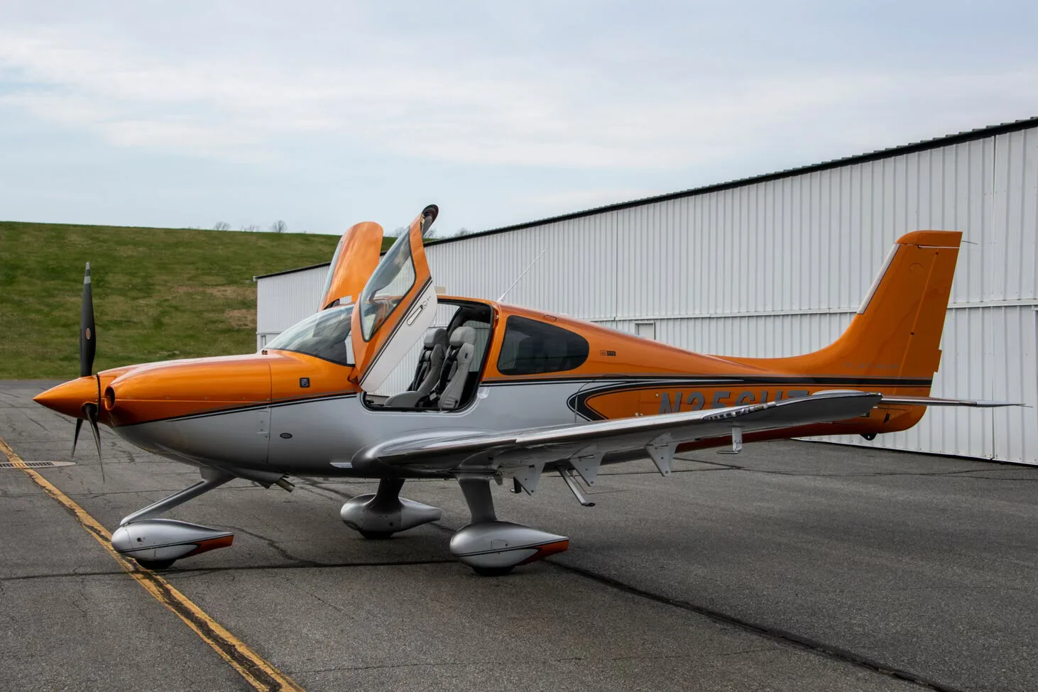 A side view of a metallic orange and silver Cirrus SR22 aircraft (N356HT) with its gull-wing doors open, parked on an asphalt ramp.