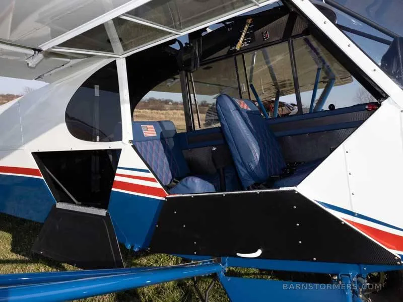The blue and red interior cabin of the Piper Super Cub, showing two seats with American flag accents and open side panels.