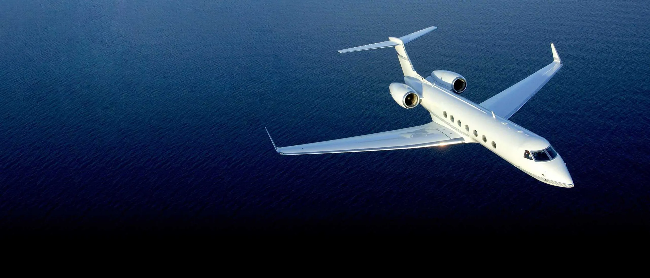 A white jet flies over the ocean.