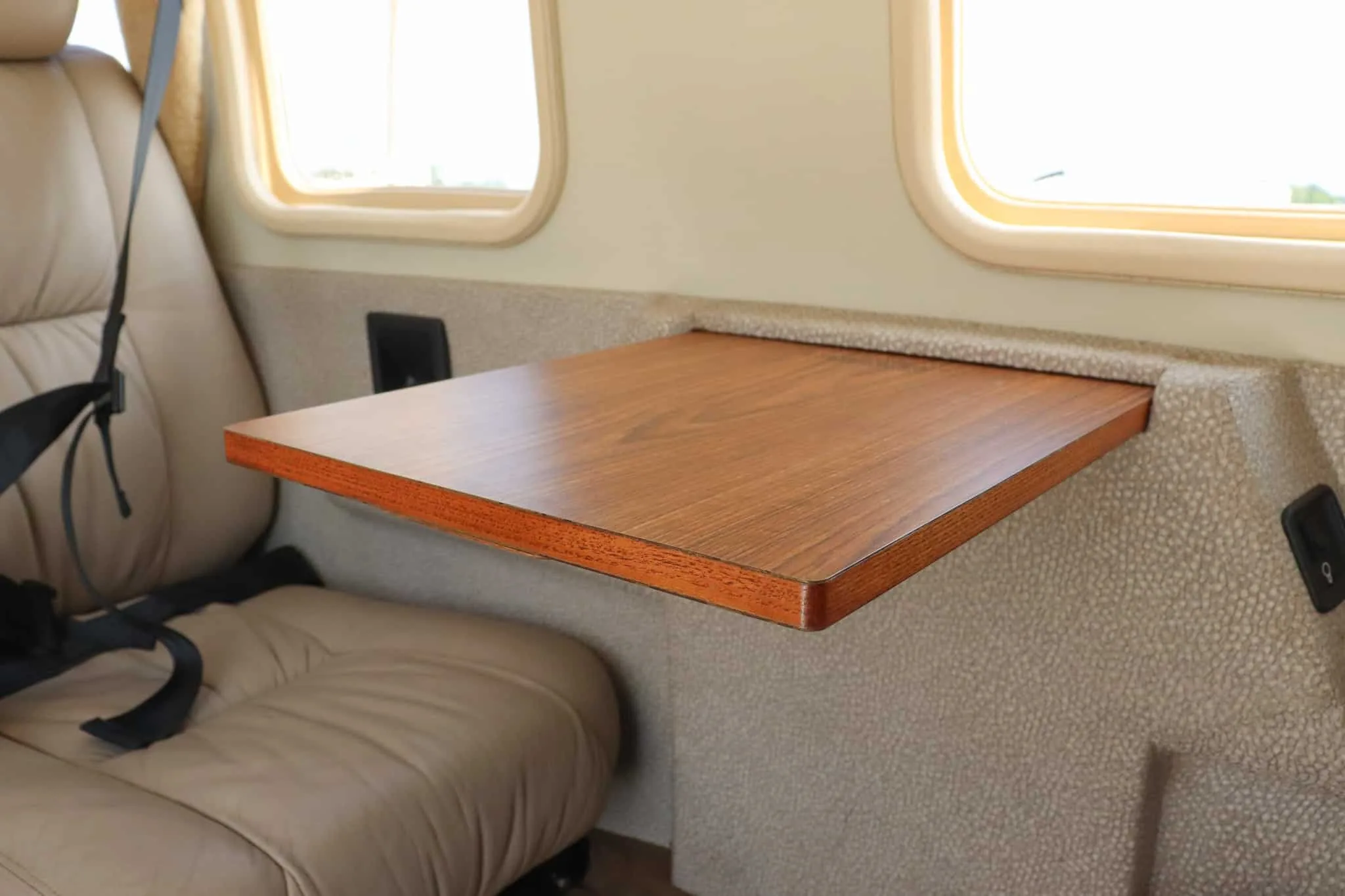 A close-up view of a light brown leather cabin seat and a wooden fold-out table inside the aircraft.
